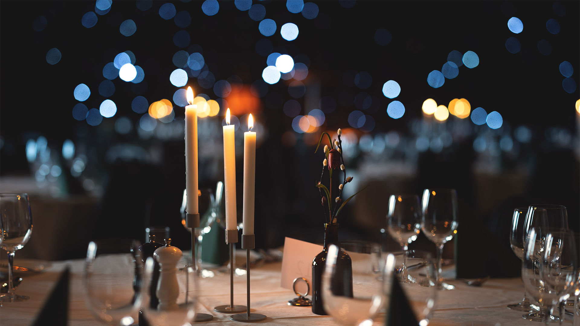 Elegant table setting with candles, wine glasses, and a bokeh effect background in a subdued atmosphere