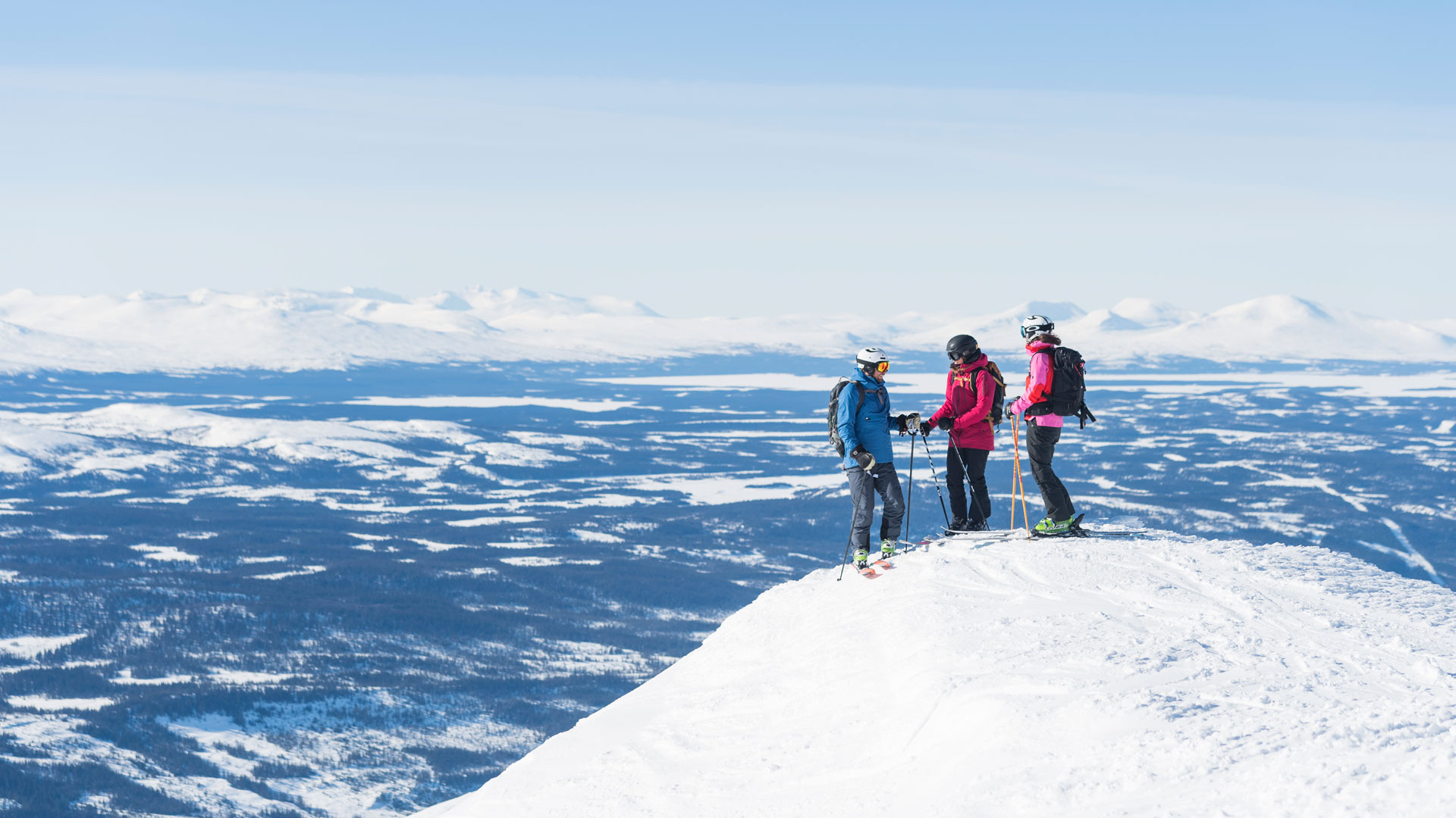 Three people skiing on a snow-covered mountain peak in the mountains under a clear blue sky