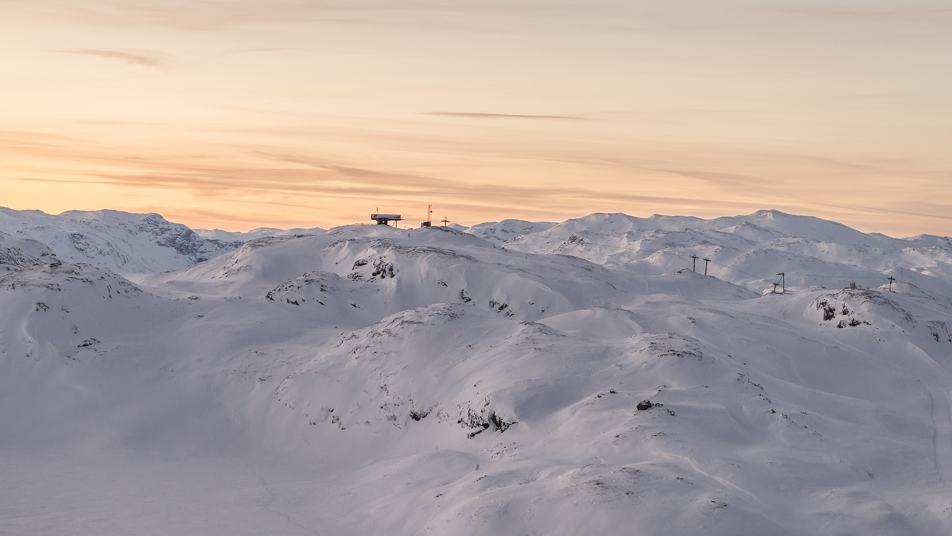Snow-covered mountain landscape at sunset with a ski lift in the background, Scandinavia