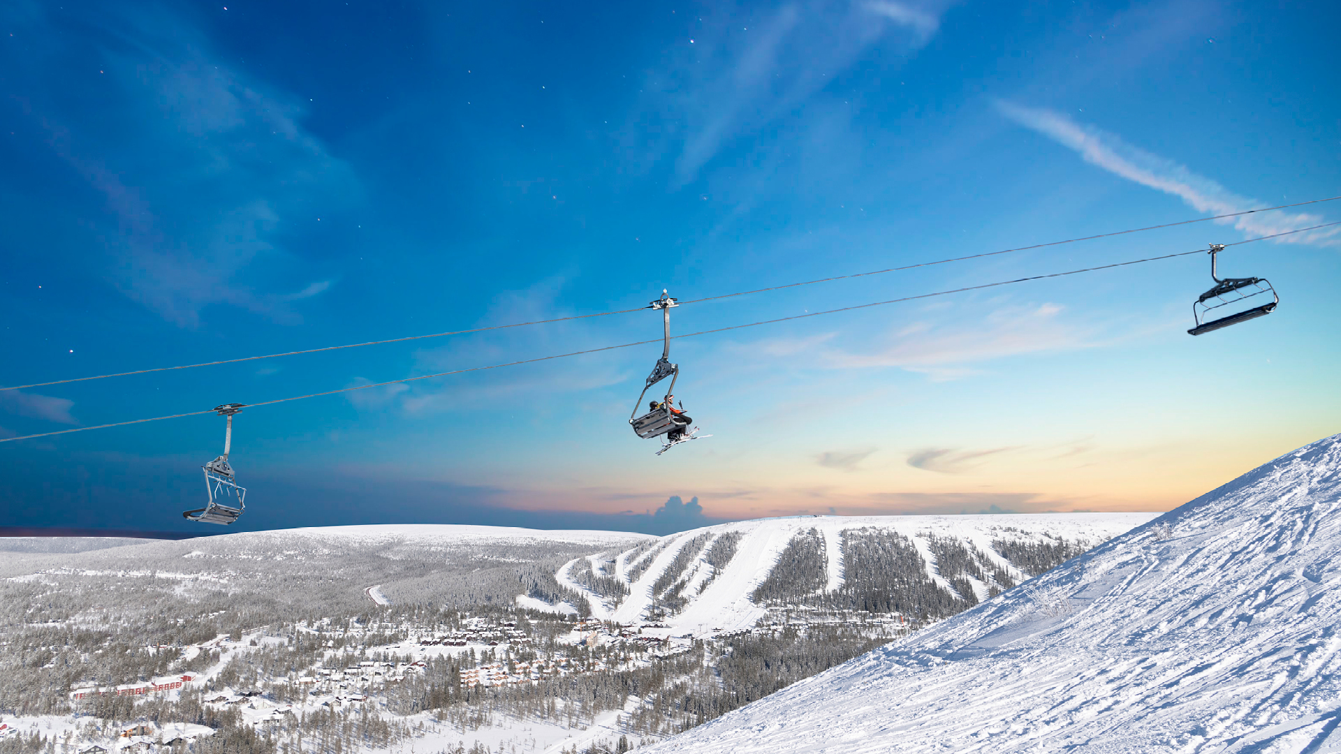 Ski resort in the mountains with snow-covered slopes and a lift under a clear sky at sunset